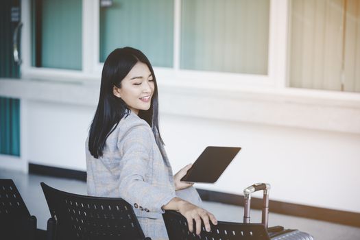 Portrait of business woman looking digital tablet with white travel bag While waiting to travel to the destination 