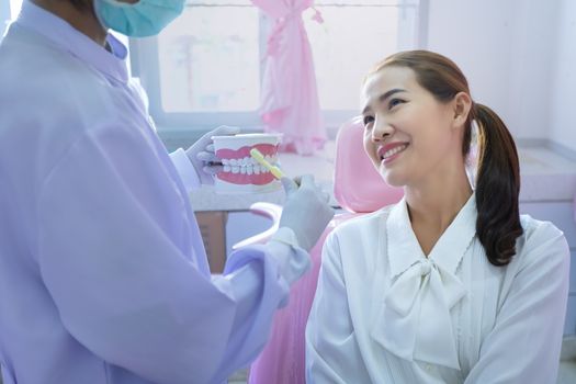 The dentist is demonstrating how to brush teeth for the patients sitting on the dental chair in her clinic.