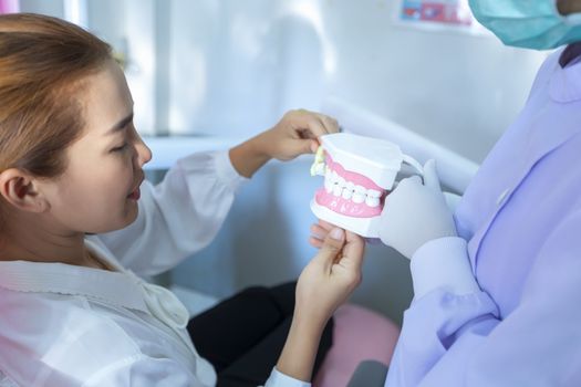The dentist is demonstrating how to brush teeth for the patients sitting on the dental chair in her clinic.