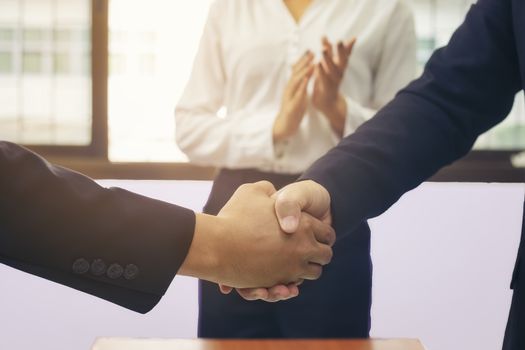 Business people shaking hands at meeting while theirs colleagues clapping and applauding. Success teamwork, partnership and handshake