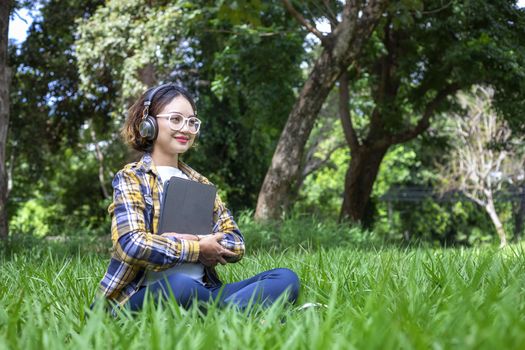 Beautiful woman listened to music while sitting happily on the lawn in the park.