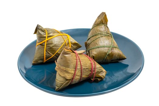 Three ZhongZi - traditional Chinese rice dish in bamboo leaves on a blue plate isolated on white