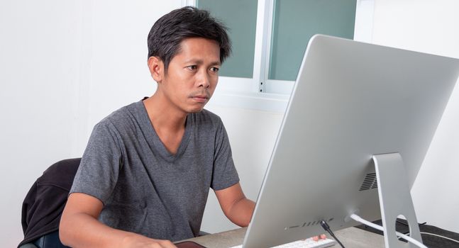Young Asian man working with desktop computer at home, Work at home because of the coronavirus epidemic ( COVID-19)