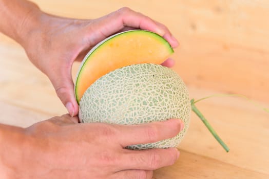 The man use knife split the orange melon on wood plate