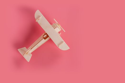 Wooden airplane toy on a pastel pink background.