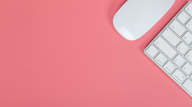 Flat lay, top view office table desk. Workspace with keyboard and mouse on pink background, banner background with copy space.