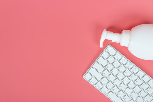 Flat lay, top view office table desk. Workspace with keyboard and hand Sanitizer on pink background.