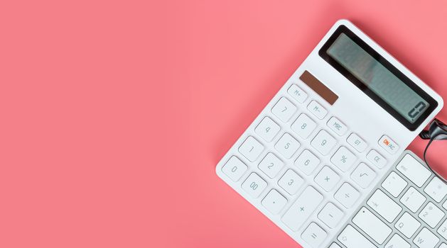 Top view female workplace, Computer keyboard, white calculator and glasses on a bright pink background.