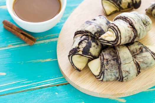 Croissant pastry with cup of coffee on vintage wooden background.