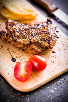 Grilled chicken steak on wooden cutting plate on black background.