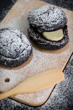 Donut with icing sugar topping on wooden plate.