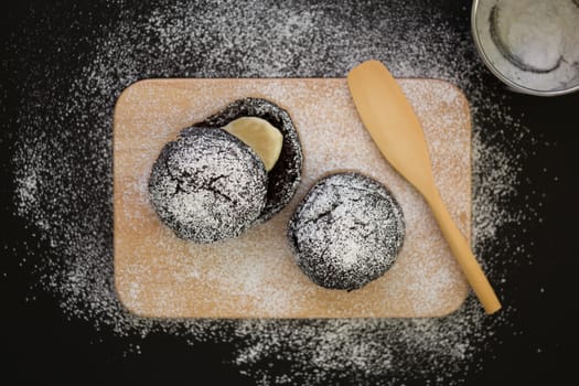 Donut with icing sugar topping on wooden plate.