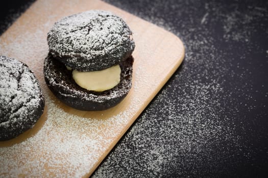 Donut with icing sugar topping on wooden plate.