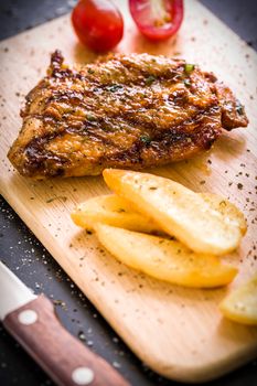 Grilled chicken steak on wooden cutting plate on black background.