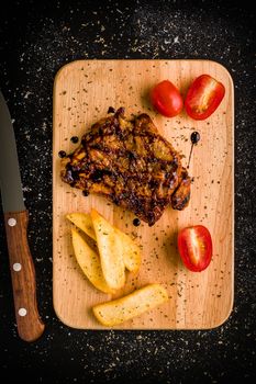 Grilled chicken steak on wooden cutting plate on black background.