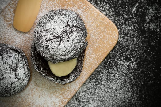 Donut with icing sugar topping on wooden plate.