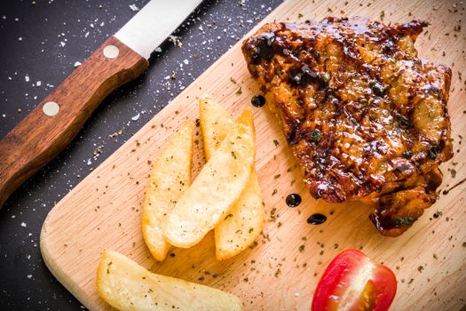 Grilled chicken steak on wooden cutting plate on black background.