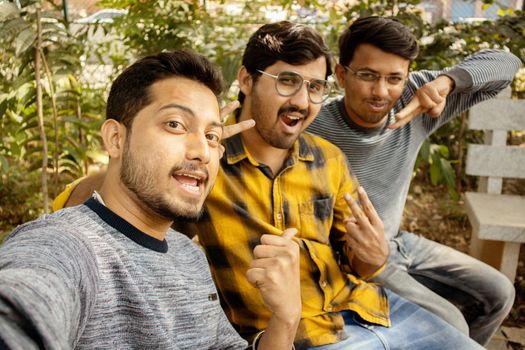 Group of friends grimacing in front of the camera - Young happy people having fun at park making funny faces while taking selfie - Concept of millennials addicted to selfie, technology and mobile