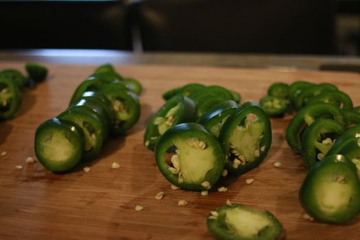Sliced fresh green and red jalapenos on a black stone board. Next to hot pepper lies a knife. Top view. Preparation for. Fermentation, cooking. Copy space.