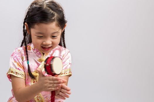 Little girl playing Chinese toy drum on white background.