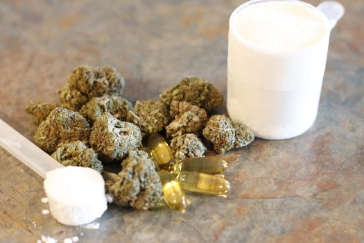 Buds of marijuana next to a scoop of protein and creatine with fish oil pills in front.