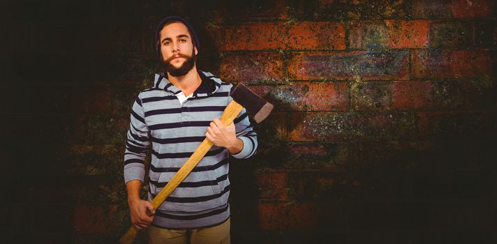 Portrait of confident hipster with hooded shirt holding axe against texture of bricks wall