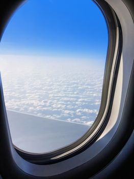 View of a commercial aeroplane from window where you can see the wing which flies above the clouds at height 35,000 feet.