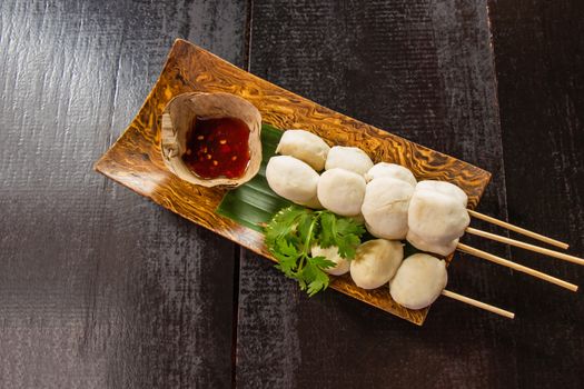 Meatballs toasted on wood dish and a cup of sauce decorated with coriander placed on the table dark wood. Top view