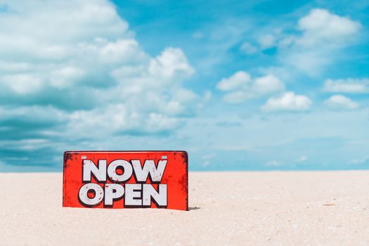 Now open sign board stand on sand summer beach background metaphor to time to travel relax tourism season with copyspace background.