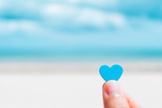 Hand hold little heart meaning feel love with summer beach with blue sky background.