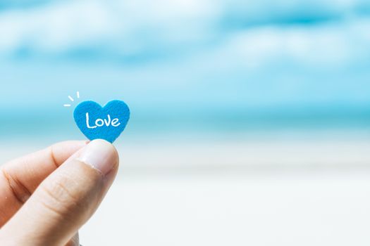 Hand hold little heart meaning feel love with summer beach with blue sky background.