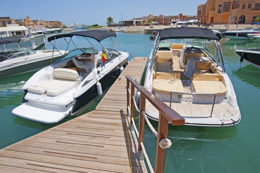 Two private motor boats moored to a wooden jetty in a tropical marina