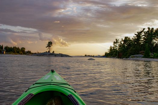 Kayaking on peaceful calm water towards setting sun. Shot from point of view of the paddler.