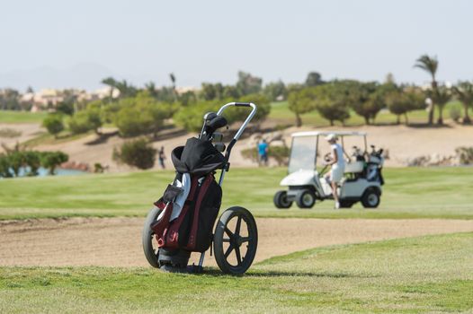 Golf caddy trolley and bag on the fairway with buggy  and bunker in the distance