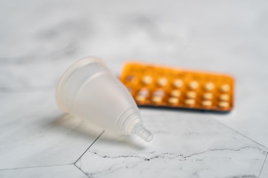 Birth control pill and menstrual cups with on white marble background.