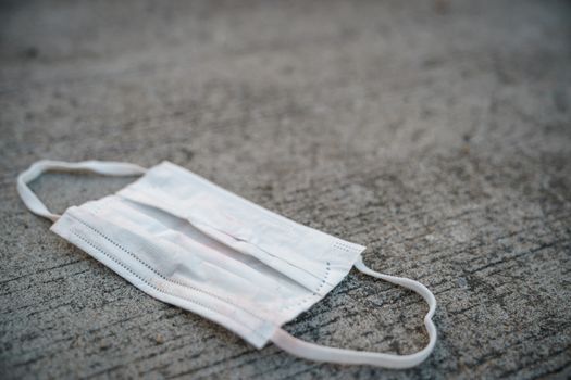 Used dirty face surgical mask dropped on the ground, selective focus center mask