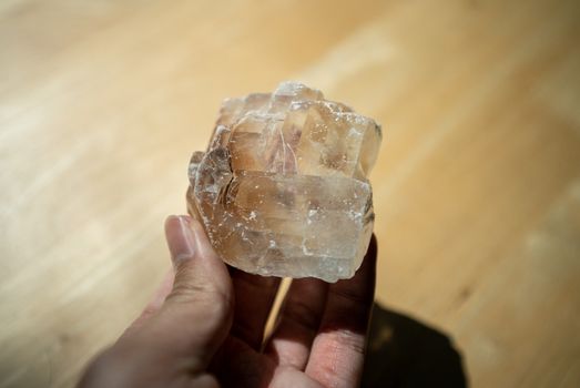 Hand holding a quartz crystal gemstone on wooden background.