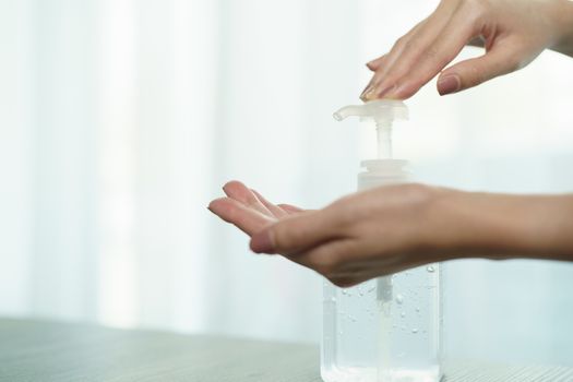 Female hands using wash hand sanitizer gel pump dispenser. Clear sanitizer in pump bottle, for killing germs, bacteria and virus.