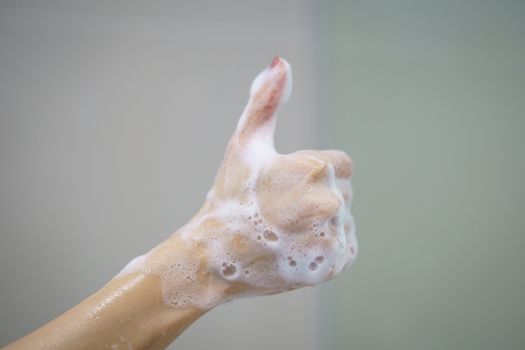 Hand with soft foam bubble from soap is showing thumbs up.