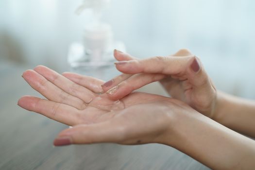 Female hands using wash hand sanitizer gel pump dispenser. Clear sanitizer in pump bottle, for killing germs, bacteria and virus.