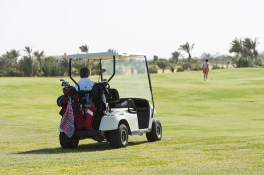 Electric golf buggy being driven on the fairway with golfer in the distance