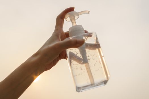 Hand with antibacterial transparent hand sanitizer gel in a plastic bottle.