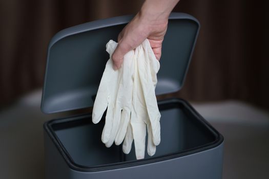 Hand putting used dirty surgical glove to a garbage bin. Mask protect dust and corona virus in trash.