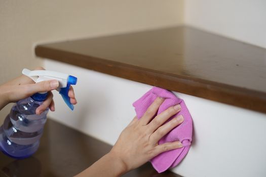 Woman hand with micro fiber cloth and detergent spray cleaning stairs at home.