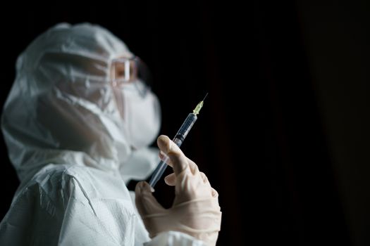 Woman wearing gloves with biohazard protective suit and mask holds an virus vaccine with syringe, for prevention and treatment from corona virus (Covid-19)