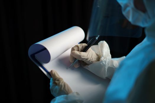 Woman wearing protective hazmat suit (PPE) and writing virus infected patient's laboratory report.