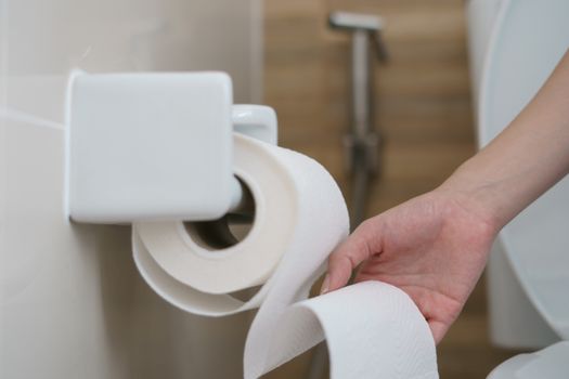 Hand pulling a roll of toilet paper tissue.