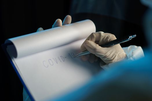 Woman wearing protective hazmat suit (PPE) and writing virus infected patient's laboratory report.