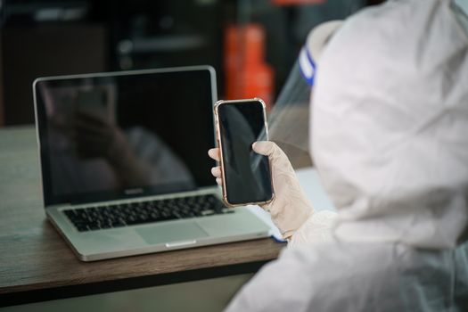 Woman in protective hazmat suit worker in laboratory computer resting and video calling on smart phone. to stop spreading coronavirus or COVID-19.