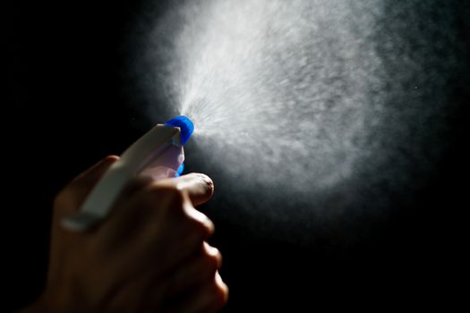 Woman's hands with blue foggy spraying disinfectant to stop spreading coronavirus or COVID-19.